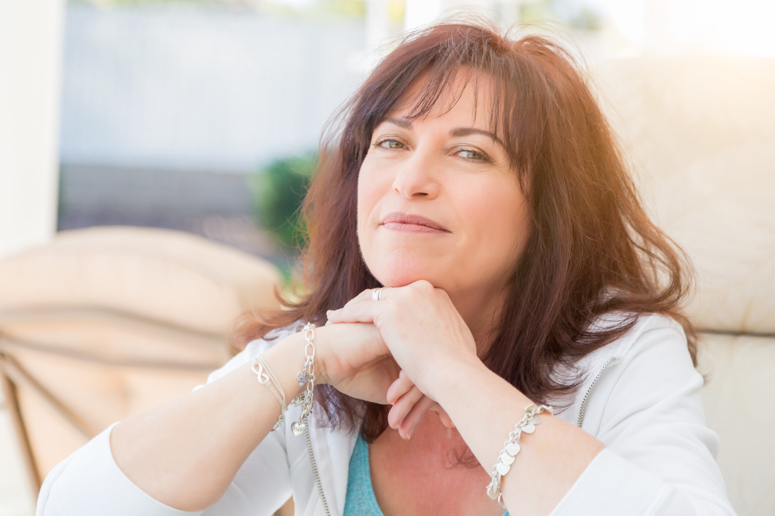 A thoughtful woman poses with her chin resting on her hands, wearing a casual outfit and silver jewelry; soft natural light enhances the serene atmosphere.